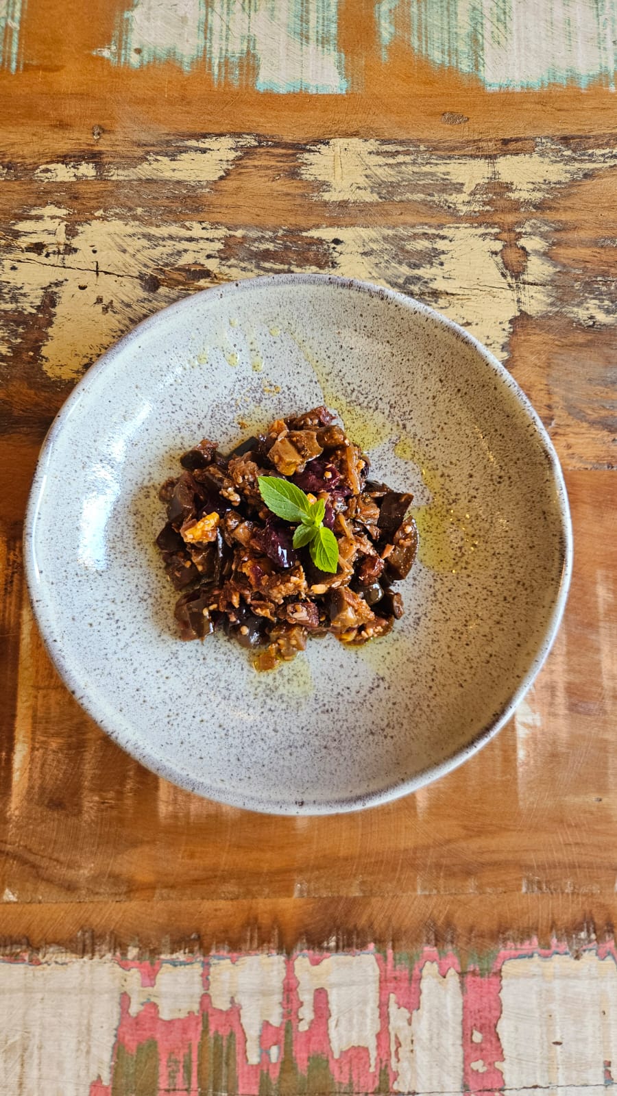 Caponata da casa servida em bowl rústico sobre mesa de madeira.
